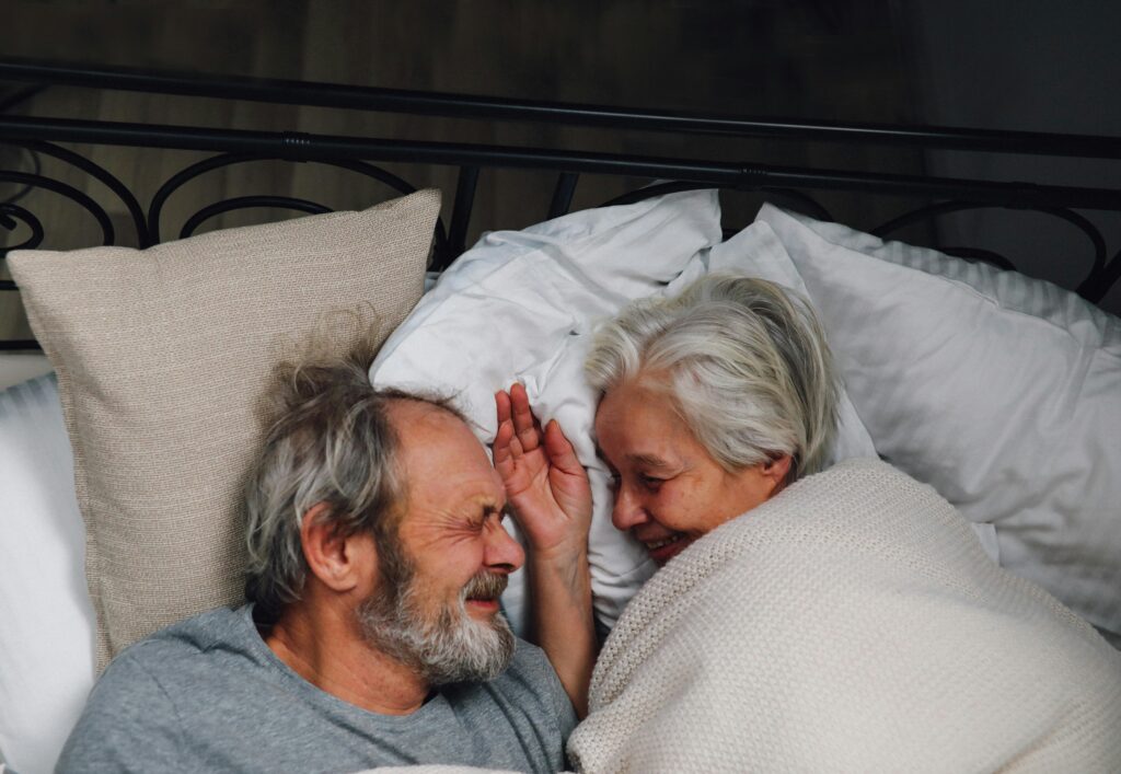 An elderly couple with silver hair happily cuddling in bed, sharing a loving and joyful moment.