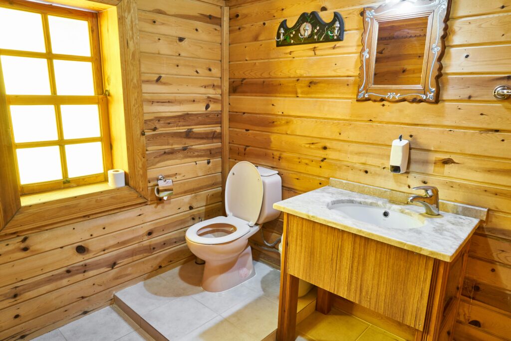 Cozy rustic bathroom with wooden design, featuring toilet and sink under warm natural light.