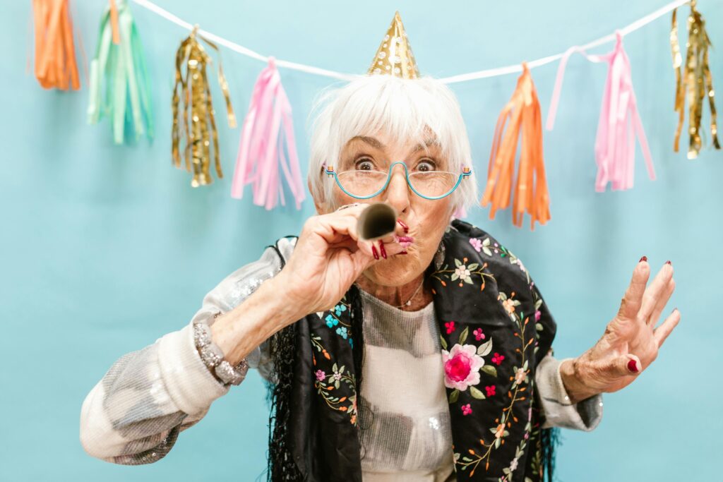 Elderly woman with eyeglasses and party hat celebrating festive occasion indoors.